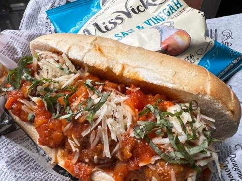 A hearty meatball sub topped with marinara sauce, shredded cheese, and fresh basil, alongside a bag of Miss Vickie's chips.