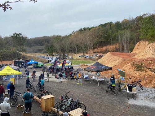 A gathering of mountain bikers at an outdoor event, with tents, bikes, and a hilly landscape in the background.