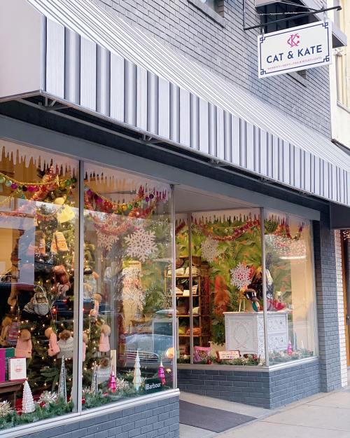 A storefront decorated for the holidays, featuring colorful displays and a sign that reads "Cat & Kate."