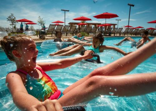 Children enjoying a fun day at the pool, floating on inner tubes and splashing water under sunny skies.