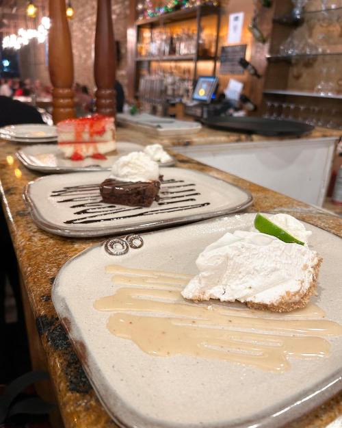 Three dessert plates on a countertop: a slice of cake, a brownie, and a pie topped with whipped cream and a lime slice.