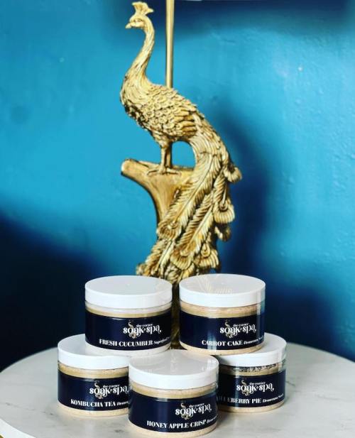 Five jars of spa products labeled with flavors like Fresh Cucumber and Carrot Cake, displayed near a decorative peacock.