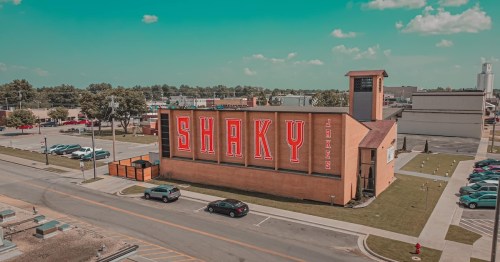 A large building with the word "SHAKY" prominently displayed on the side, surrounded by a parking lot and trees.