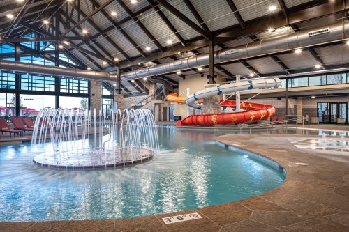 Indoor water park featuring a pool, water slide, and splash area with fountains and lounge chairs.