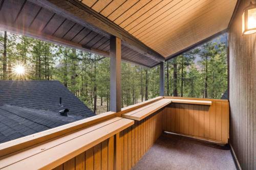 A cozy balcony with wooden railings overlooks a forest at sunset, with warm light filtering through the trees.