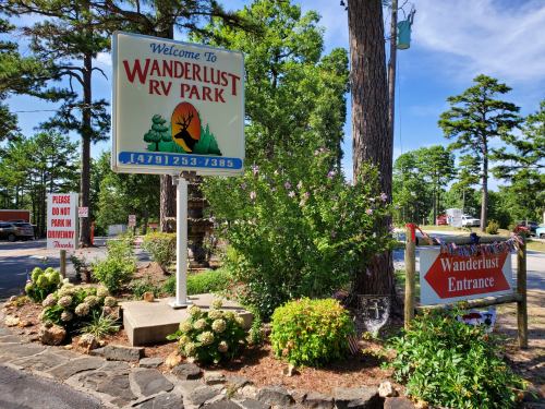 Sign for Wanderlust RV Park with flowers and trees, indicating the entrance and parking instructions.