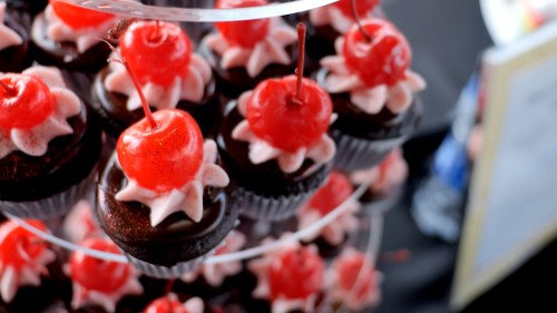 A display of chocolate cupcakes topped with pink frosting and bright red cherries.