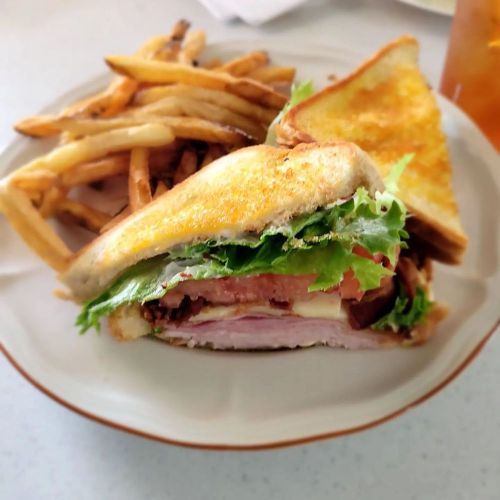 A plate with a sandwich filled with lettuce, tomato, and ham, accompanied by a side of golden fries and toast.