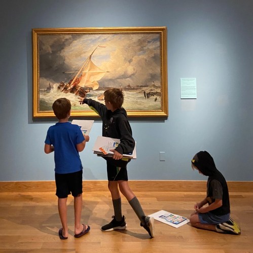 Three children observe a painting in a gallery, one pointing at the artwork while others take notes.