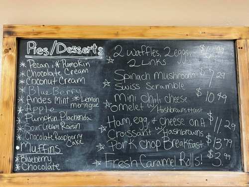 Chalkboard menu listing pies, desserts, and breakfast items with prices, including waffles, omelets, and muffins.