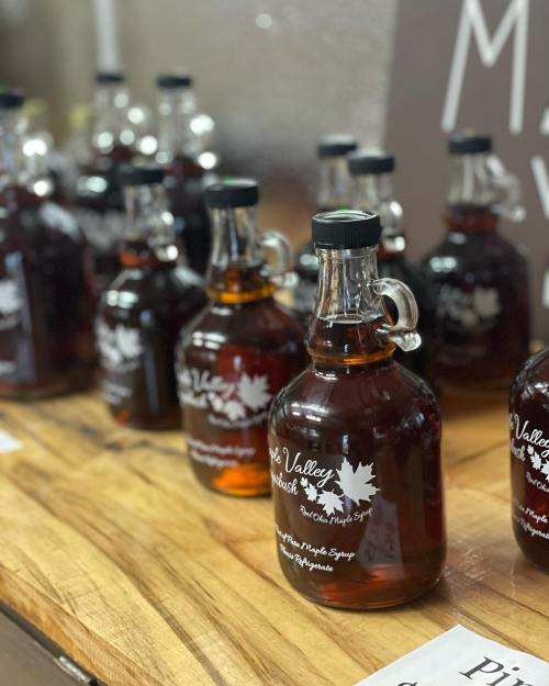 Bottles of maple syrup lined up on a wooden table, with labels featuring a maple leaf design.