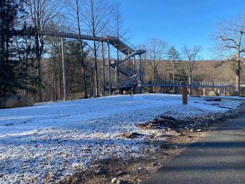A snowy landscape featuring a large, winding slide structure surrounded by trees and a clear blue sky.