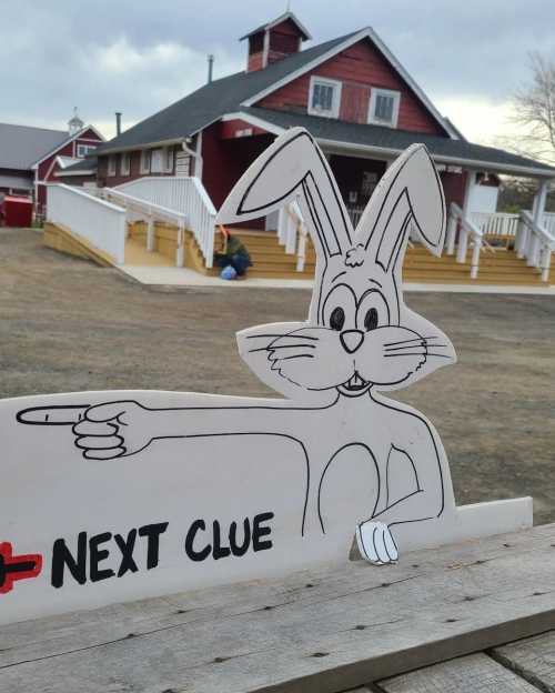 A cartoon rabbit pointing to a sign that says "NEXT CLUE" in front of a red barn and cloudy sky.