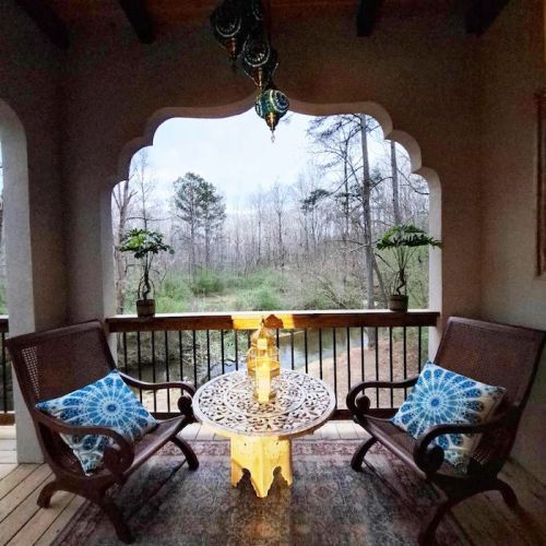 Cozy porch with two chairs, a decorative table, and lanterns, overlooking a serene wooded landscape.