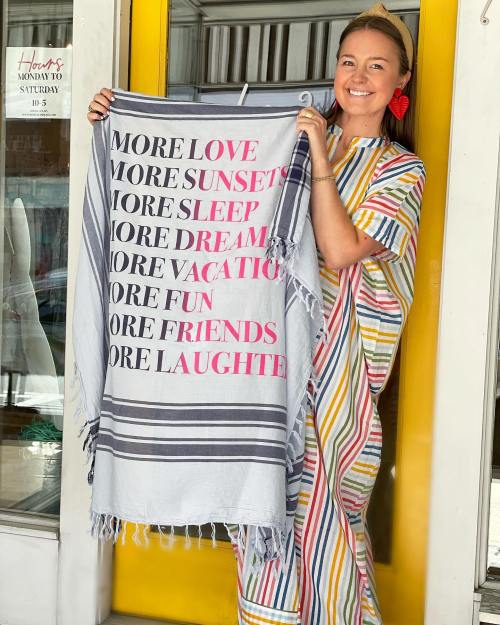 A woman in a colorful striped dress holds a blanket with the text "More Love, Sunsets, Sleep, Dream, Vacation, Fun, Friends, Laughter."