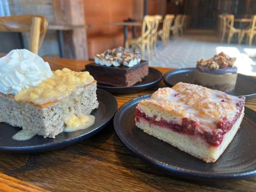 A variety of desserts on dark plates, including a cake with cream, a brownie, and a fruit bar, set in a cozy café.