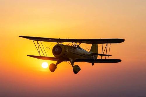 A vintage biplane flying against a vibrant sunset sky.
