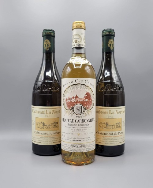 Three wine bottles: two red from Château La Nerthe and one white from Château Carbonnieux, all elegantly displayed.