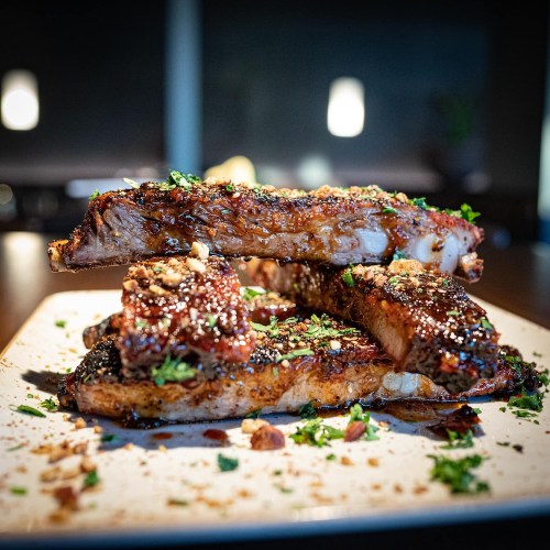 A close-up of succulent, glazed ribs garnished with herbs and spices, arranged on a white plate.