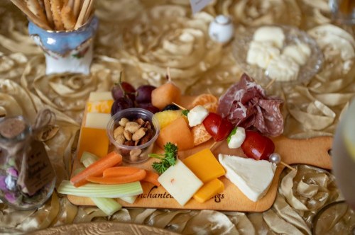 A wooden platter with assorted cheeses, meats, fruits, nuts, and vegetables on a golden tablecloth.