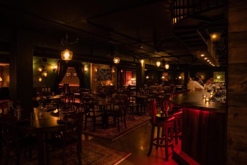 Cozy restaurant interior with dim lighting, wooden tables, and a bar, featuring elegant decor and a warm atmosphere.