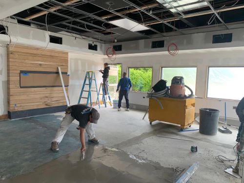 Workers renovating a room, with one applying concrete, another on a ladder, and a third installing fixtures.