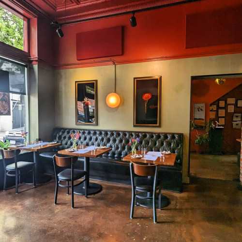 Cozy restaurant interior with wooden tables, chairs, and framed artwork on the walls, featuring warm lighting.