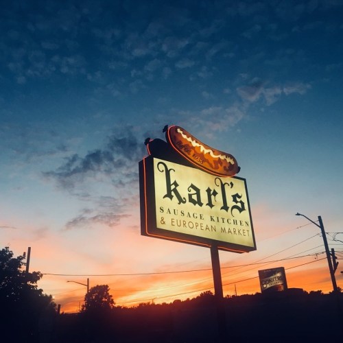 Sign for Karl's Sausage Kitchen & European Market against a colorful sunset sky.
