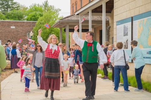 A festive crowd celebrates with Norwegian flags, featuring adults in traditional attire and children enjoying the event.