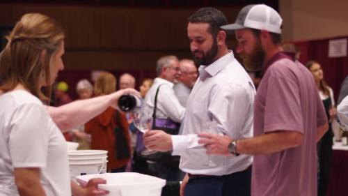 A group of people at a wine tasting event, with one person pouring wine into a glass.