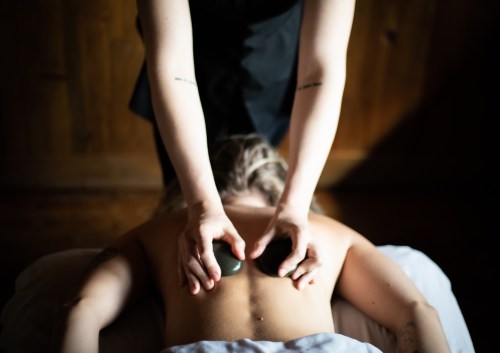 A person receiving a hot stone massage, with hands applying stones to their back in a serene setting.