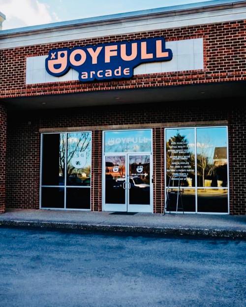 Exterior of Joyfull Arcade, featuring large signage and glass doors reflecting the surroundings.