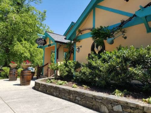 A colorful building with teal accents, surrounded by greenery and flower planters, on a sunny day.