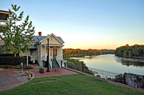 A serene riverside view at sunset, featuring a charming house and a bridge in the background.