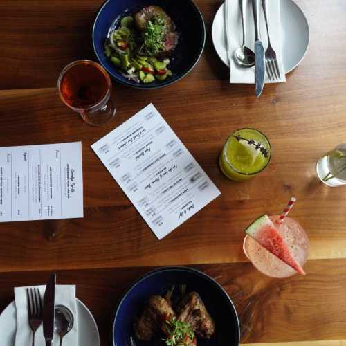 A wooden table with two plates of food, drinks, and a menu, set for a meal.