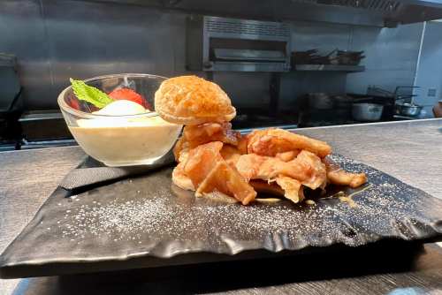 A plate with apple pie filling, a biscuit, and a bowl of vanilla ice cream garnished with mint and a strawberry.