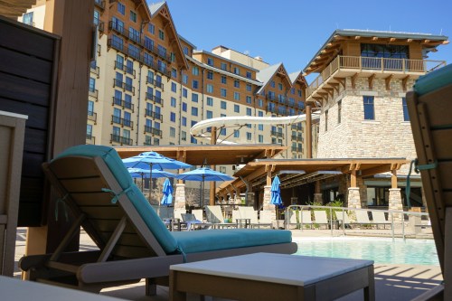 A poolside view featuring lounge chairs, umbrellas, and a modern hotel building in the background.