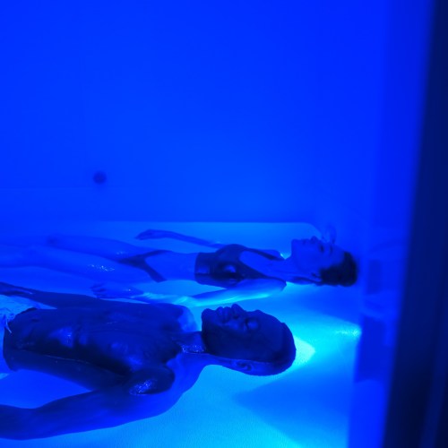 Two people floating in a blue-lit water environment, appearing relaxed and serene.