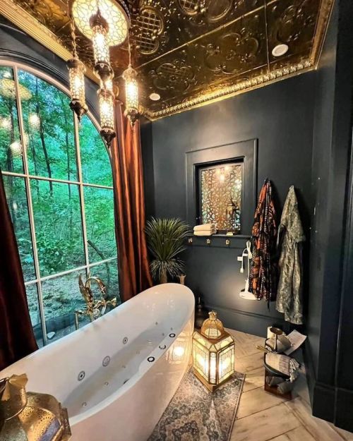 Luxurious bathroom with a freestanding tub, ornate ceiling, lanterns, and large window overlooking greenery.
