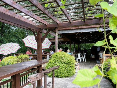 A cozy outdoor dining area with wooden structures, colorful umbrellas, and guests enjoying a meal amidst greenery.
