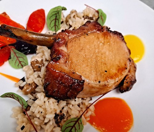 A beautifully plated pork chop on a bed of rice, garnished with colorful sauces and fresh greens.