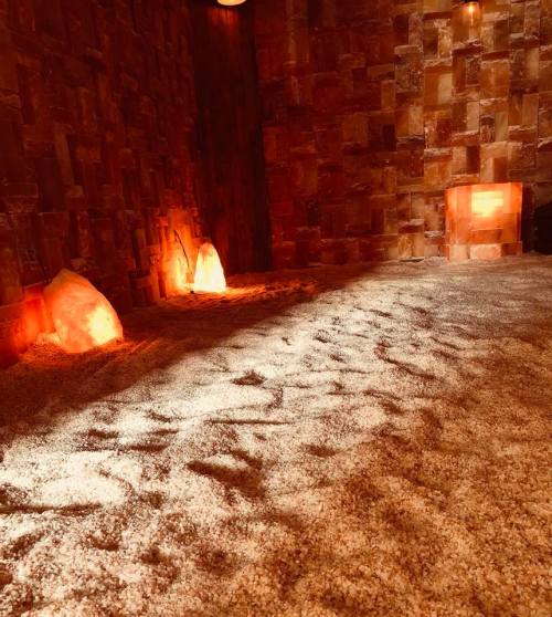 A serene room with salt walls, glowing salt lamps, and a sandy floor, creating a calming atmosphere.