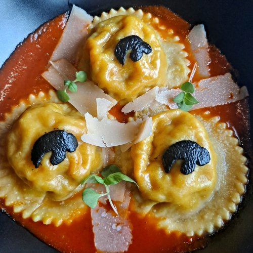 Three ravioli in a rich red sauce, topped with black truffle slices and garnished with microgreens and cheese shavings.