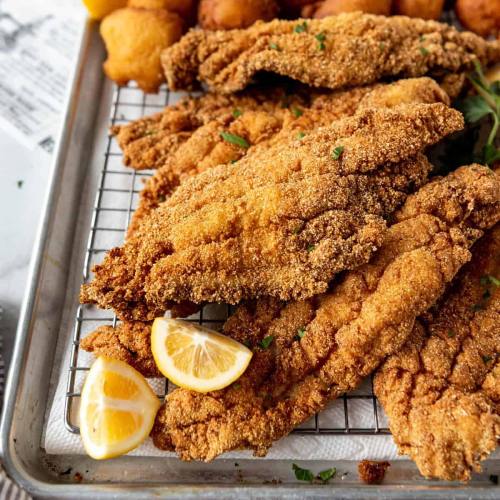 Crispy fried fish fillets on a tray, garnished with lemon slices and served with golden-brown fritters.