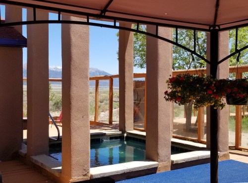 A serene outdoor space featuring a small pool, surrounded by columns and greenery, with mountains in the background.