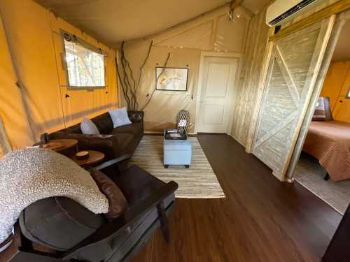 Cozy interior of a glamping tent featuring a sofa, coffee table, and a bedroom area with warm lighting.