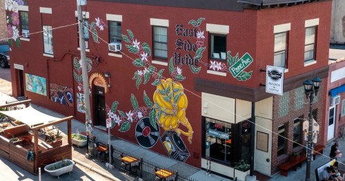 Colorful mural on a brick building featuring flowers and vinyl records, with outdoor seating below.