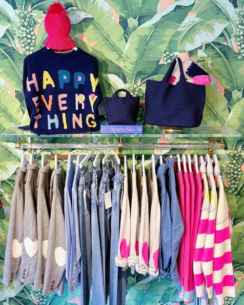 Colorful clothing display featuring sweaters, denim, and accessories against a tropical leaf backdrop.
