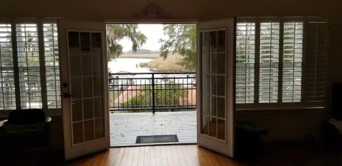 View from an open doorway showing a serene waterfront scene with trees and a railing.