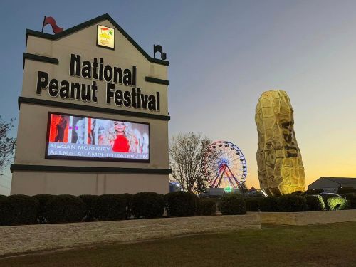 Sign for the National Peanut Festival with a large peanut sculpture, a ferris wheel, and a digital display at sunset.
